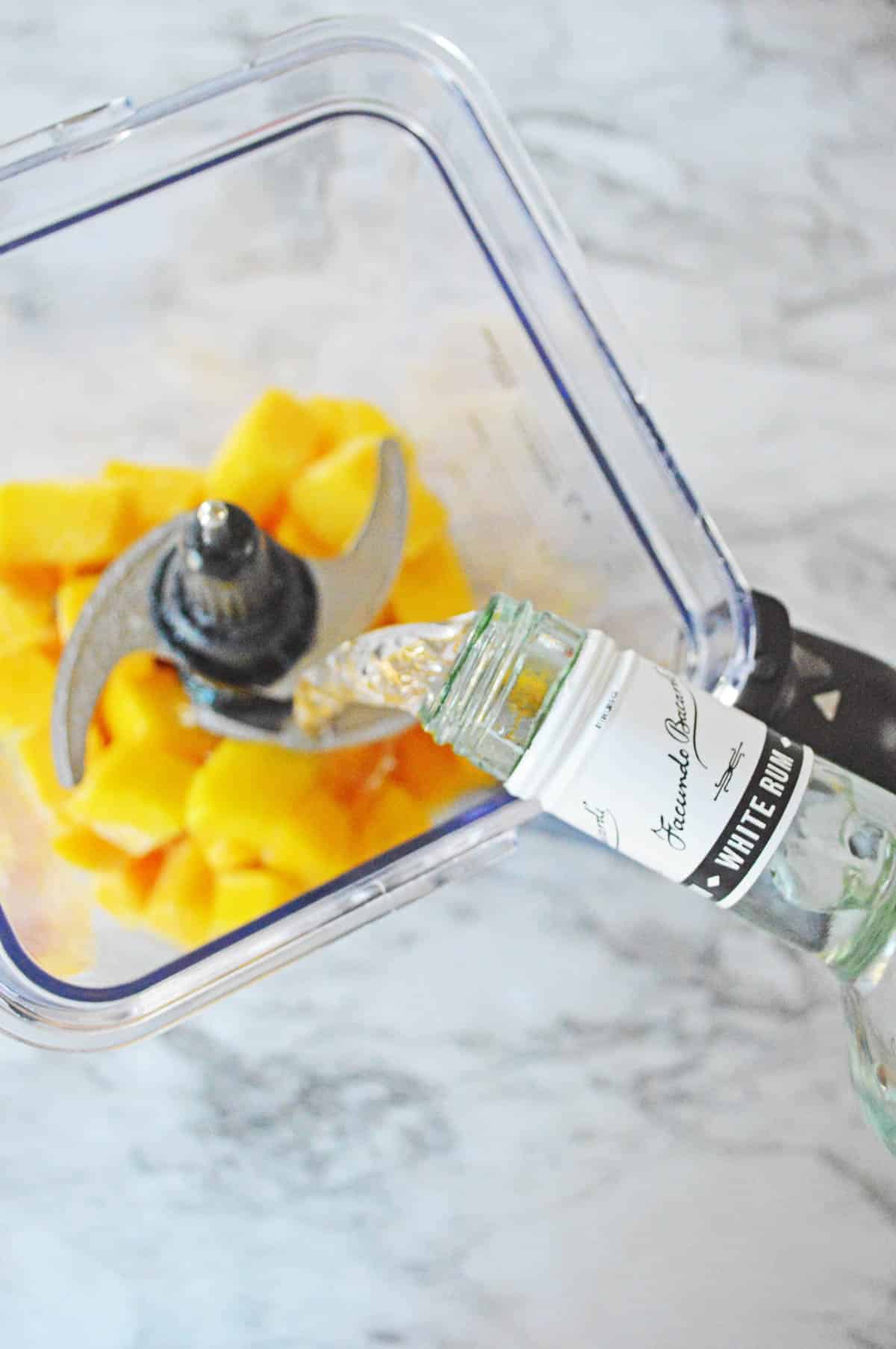 Adding rum to frozen mango in a blender.