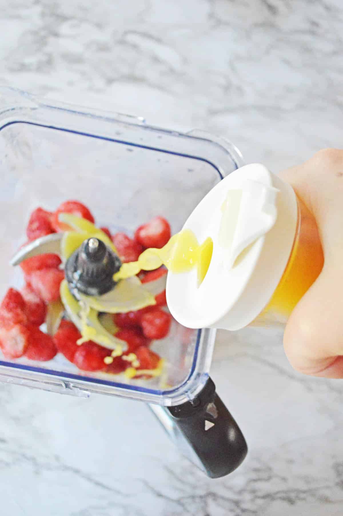 Adding orange juice to frozen strawberries in a blender.