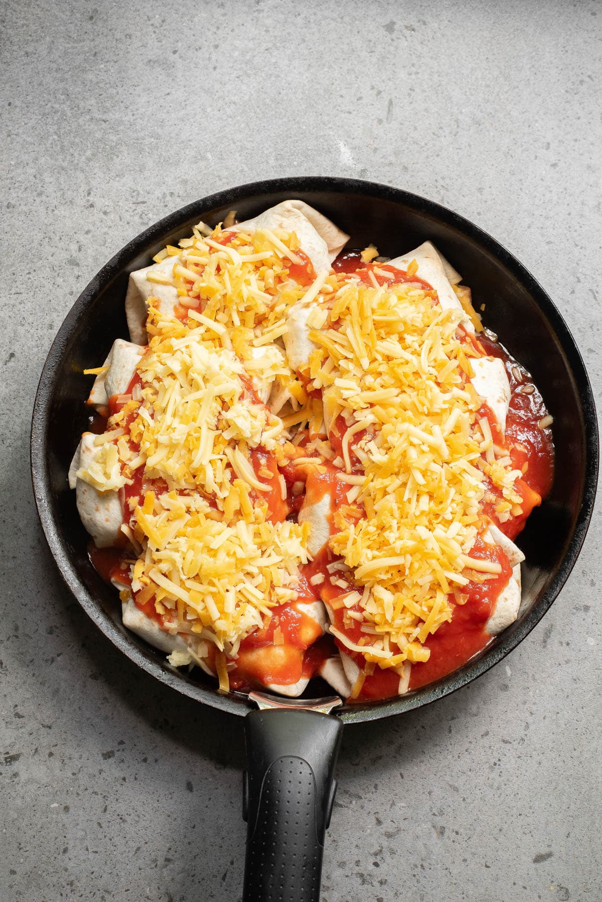 Tortillas folded and covered in sauce and cheese in a cast iron skillet.
