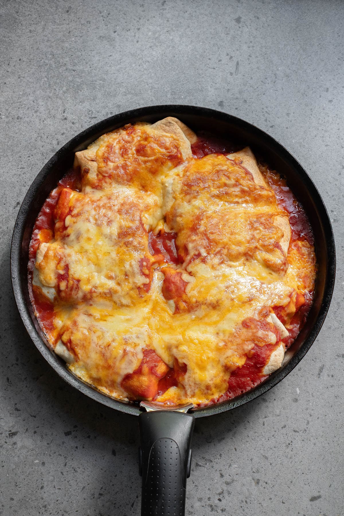 Baked tortillas folded and covered in sauce and melted cheese in a cast iron skillet.