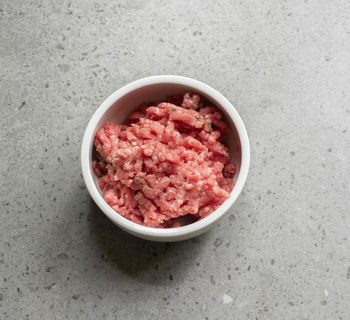 Ground beef in a white bowl on a gray counter.