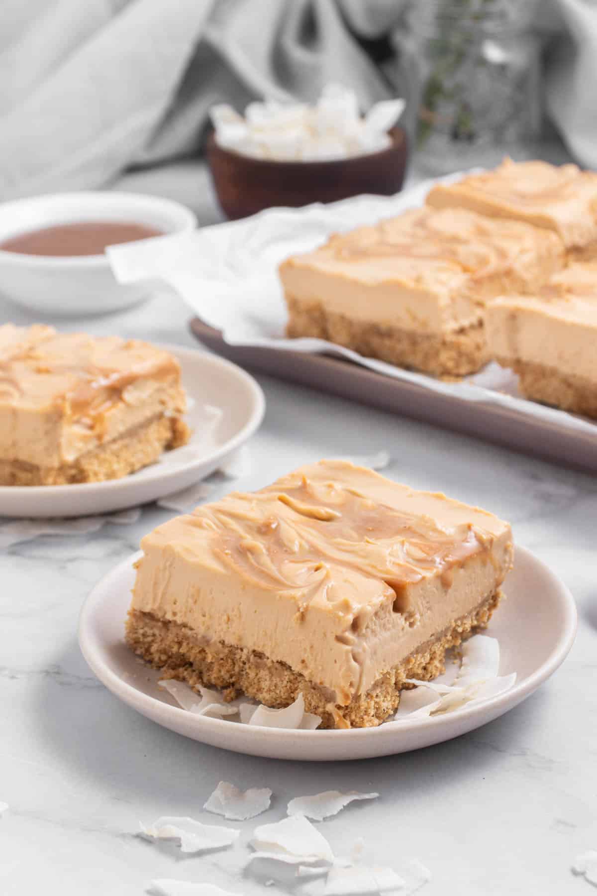 Cheesecake slices on a white plate with a small bowl of caramel in the background.
