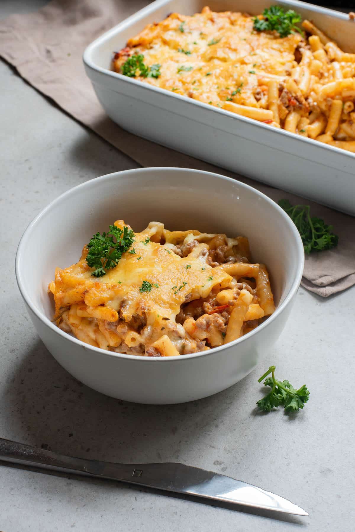 White bowl of baked ziti dish topped with cheese.