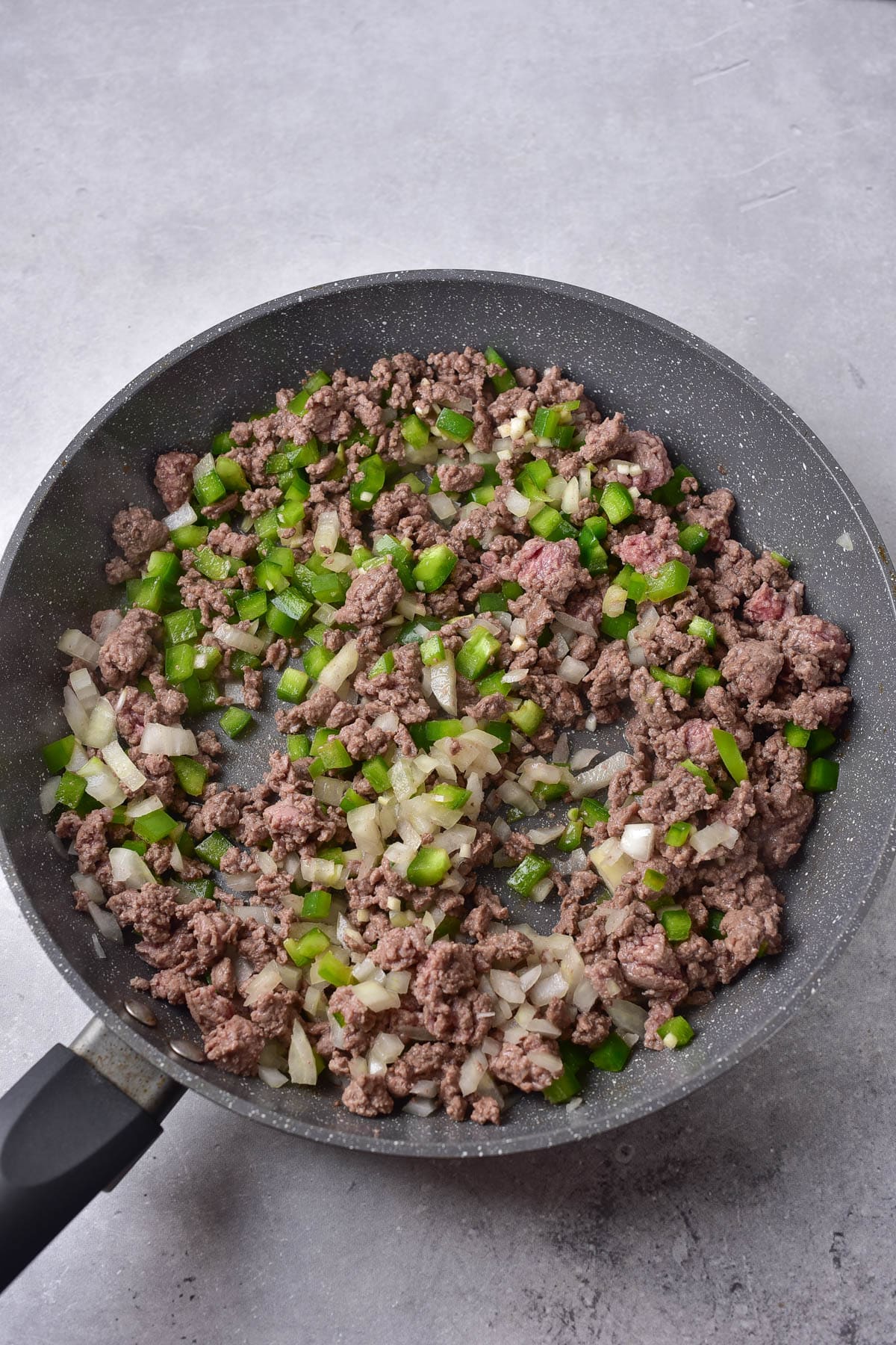 Ground beef in a skillet with onions, garlic, and peppers.