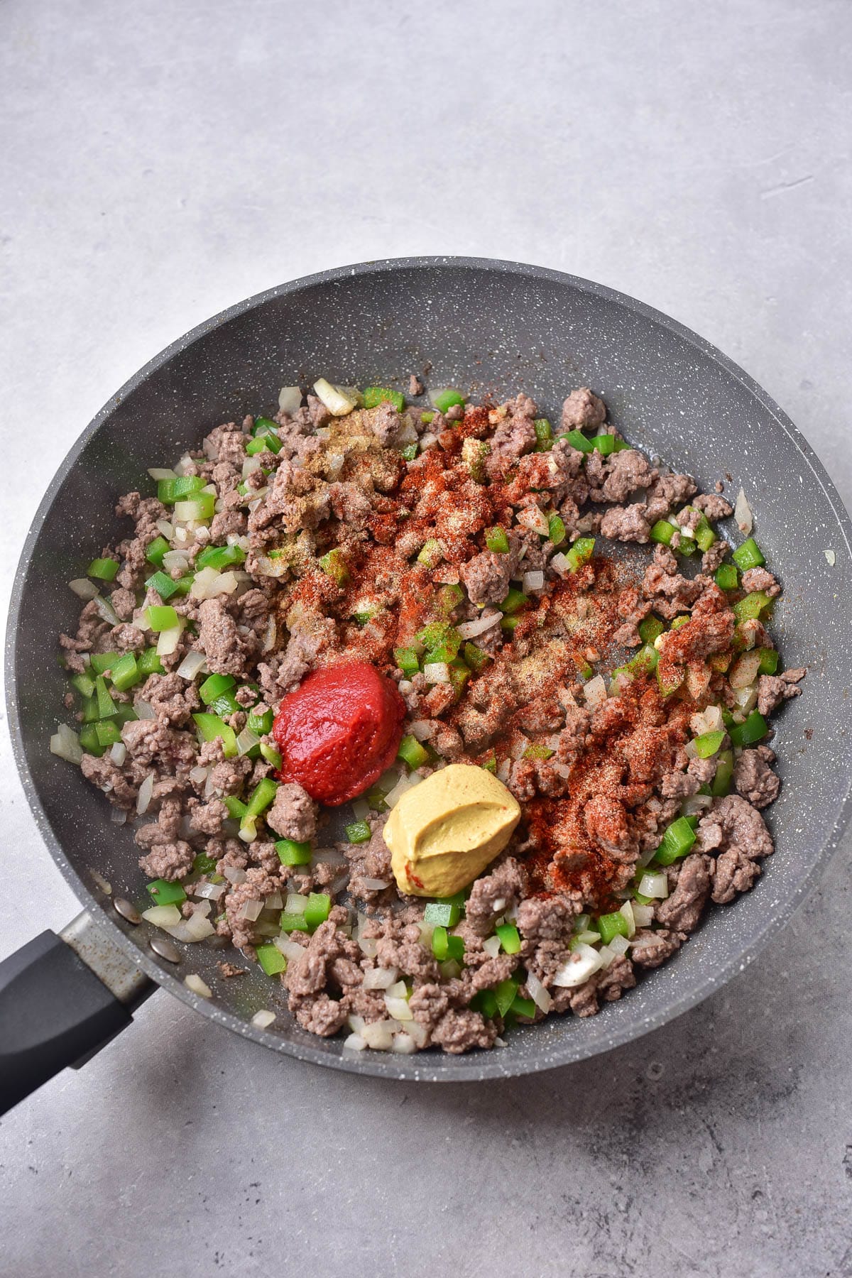 Ground beef in a skillet with onions, garlic, peppers, tomato paste and mustard.