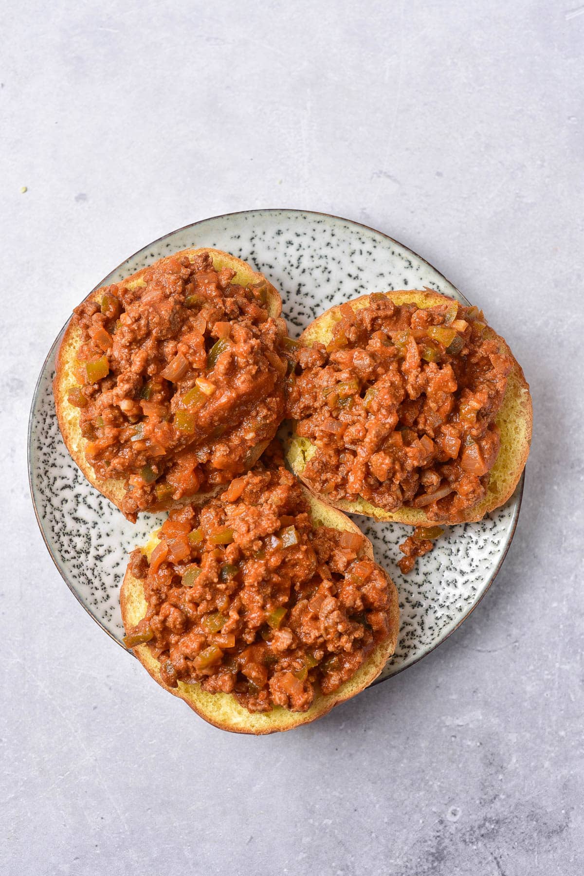Ground beef with tomato based sauce on the bottoms of hamburger buns.