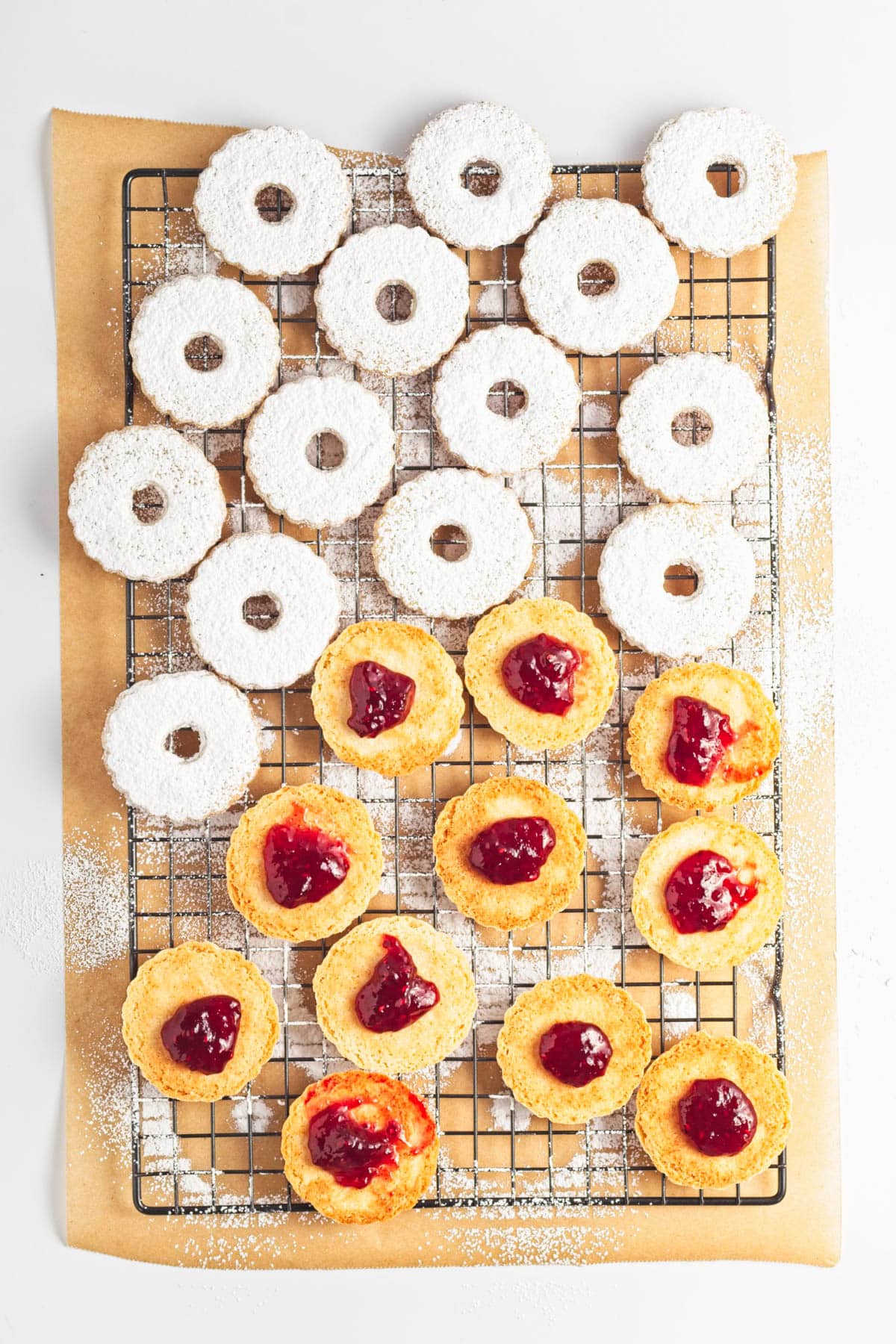 Cookies with jam and powdered sugar on a cookie rack over parchment paper.