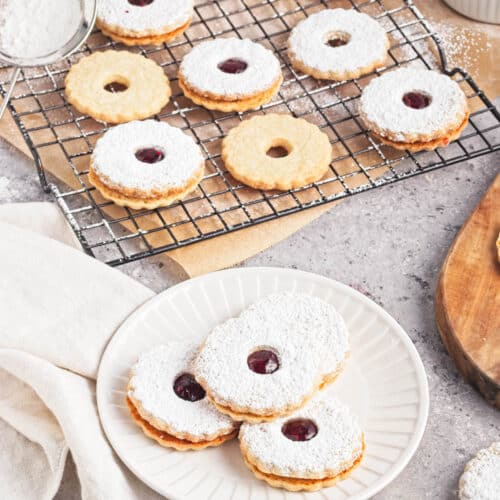 Cookies with jam and powdered sugar on a white plate on napkin with more cookies in background.
