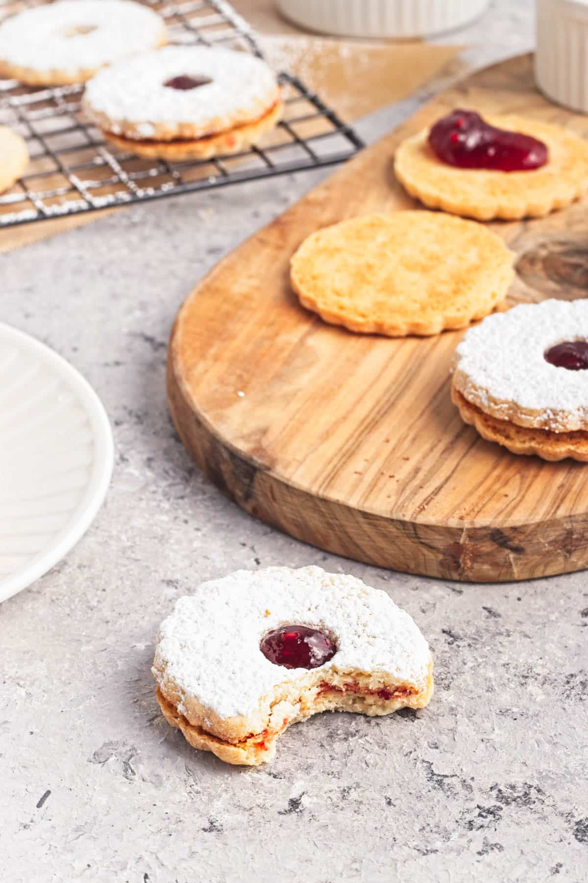 Cookies with jam and powdered sugar on a white plate on napkin with more cookies in background.