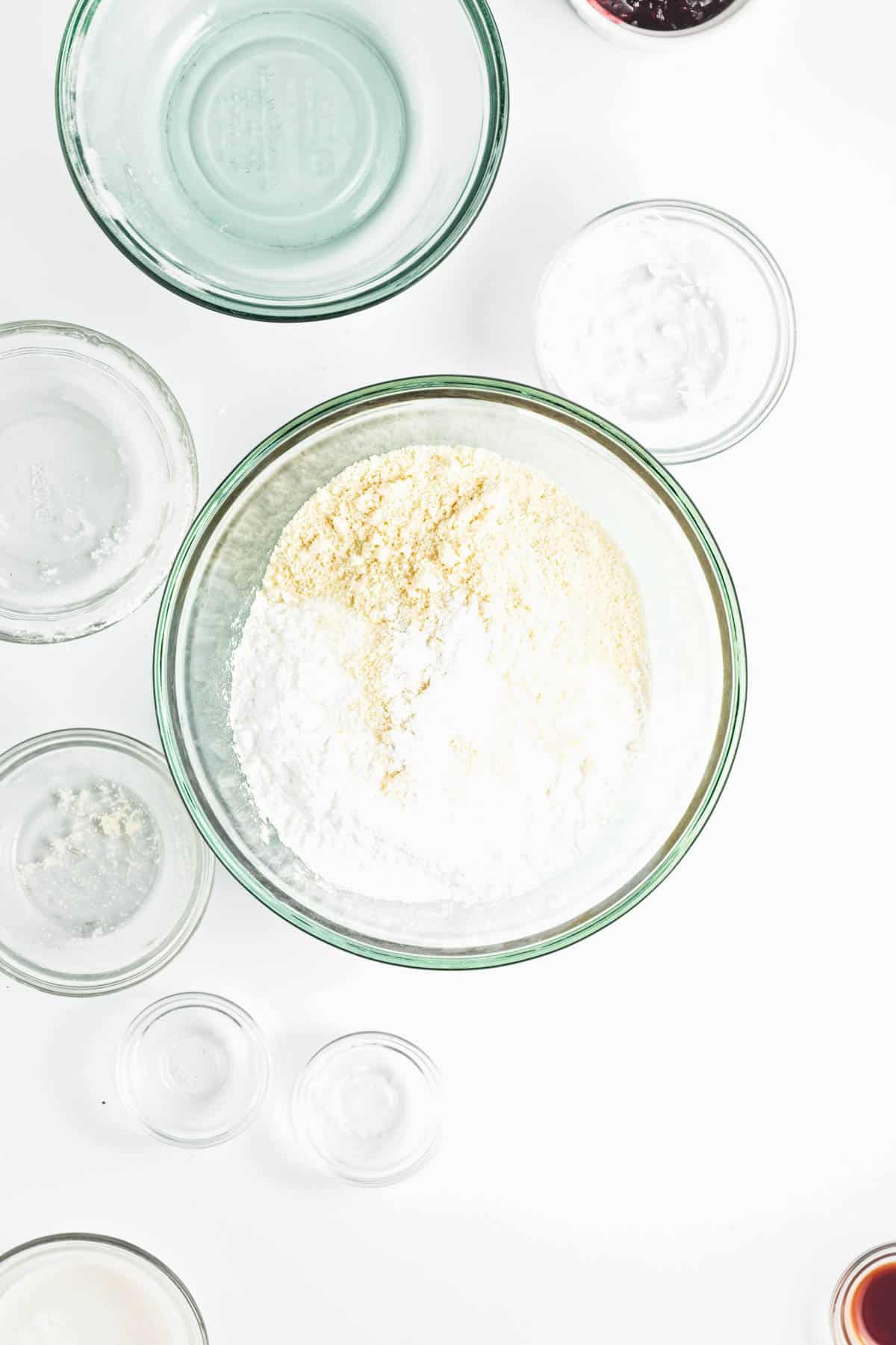 Almond and all-purpose flours in a glass bowl with other ingredients to the sides.