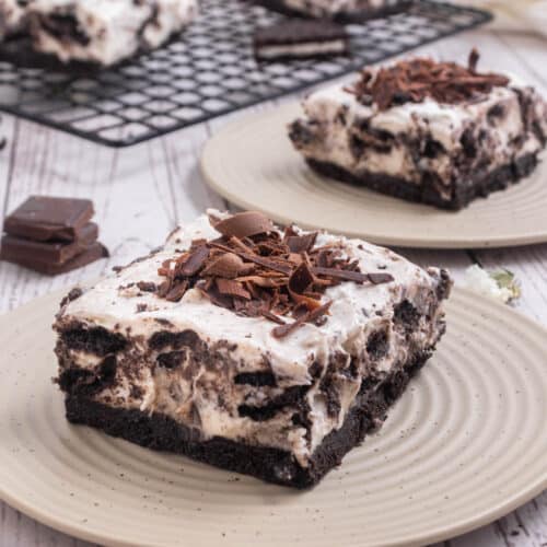 Oreo cheesecake bar on a white plate with more cheesecake in background.