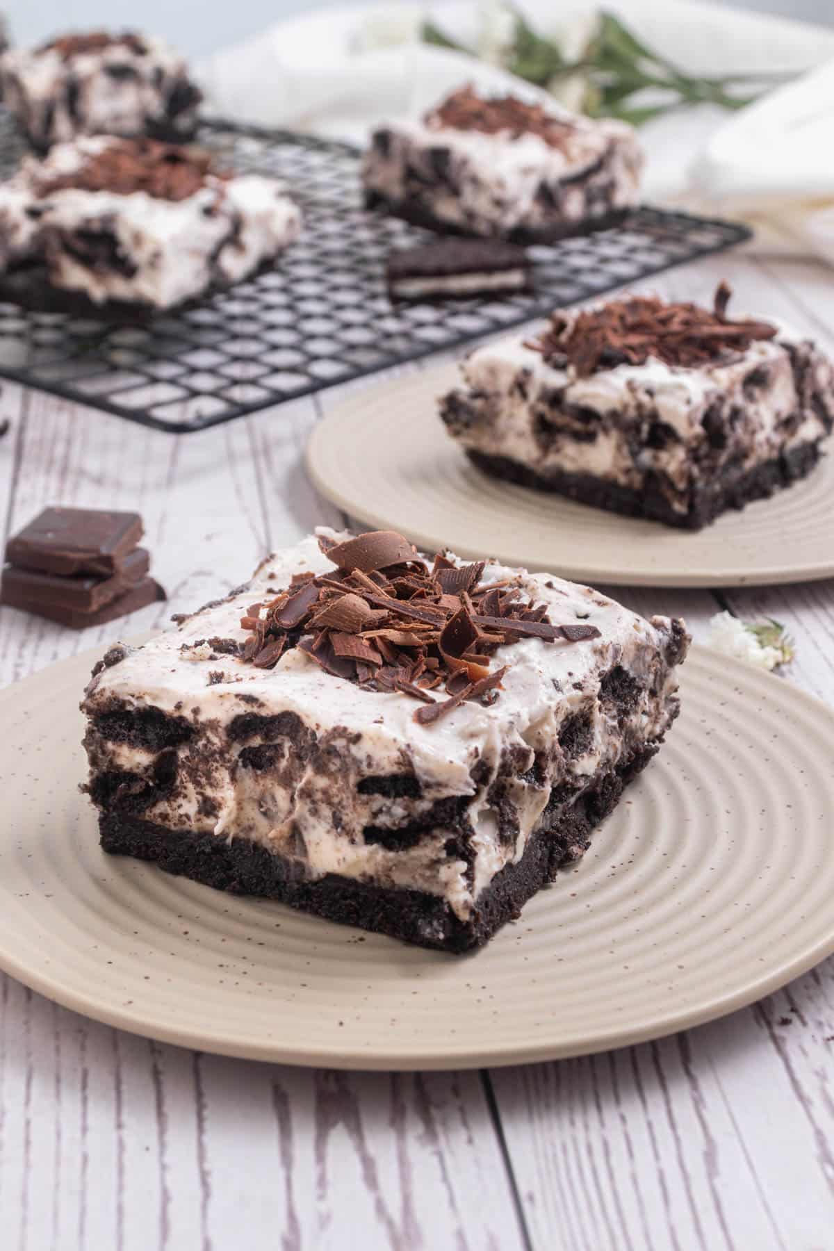 Oreo cheesecake bar on a white plate with more cheesecake in background.