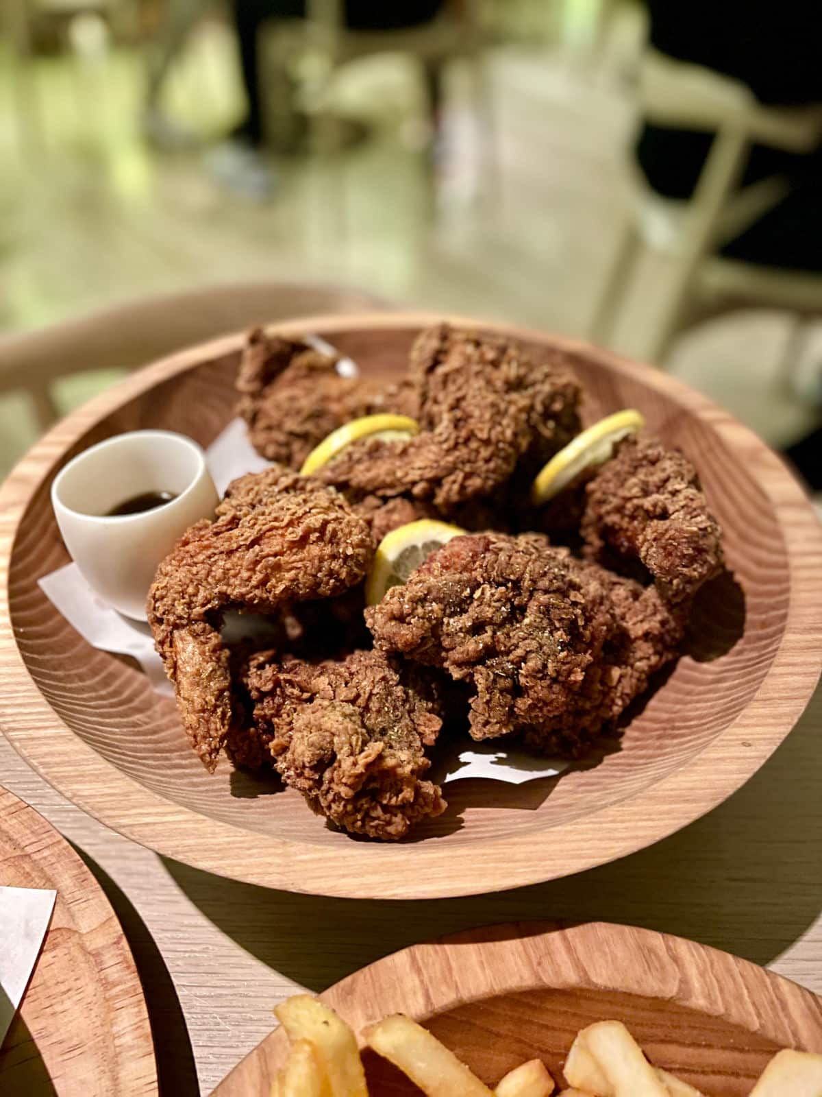 Fried chicken in a wood bowl with a dish of sauce and lemons.