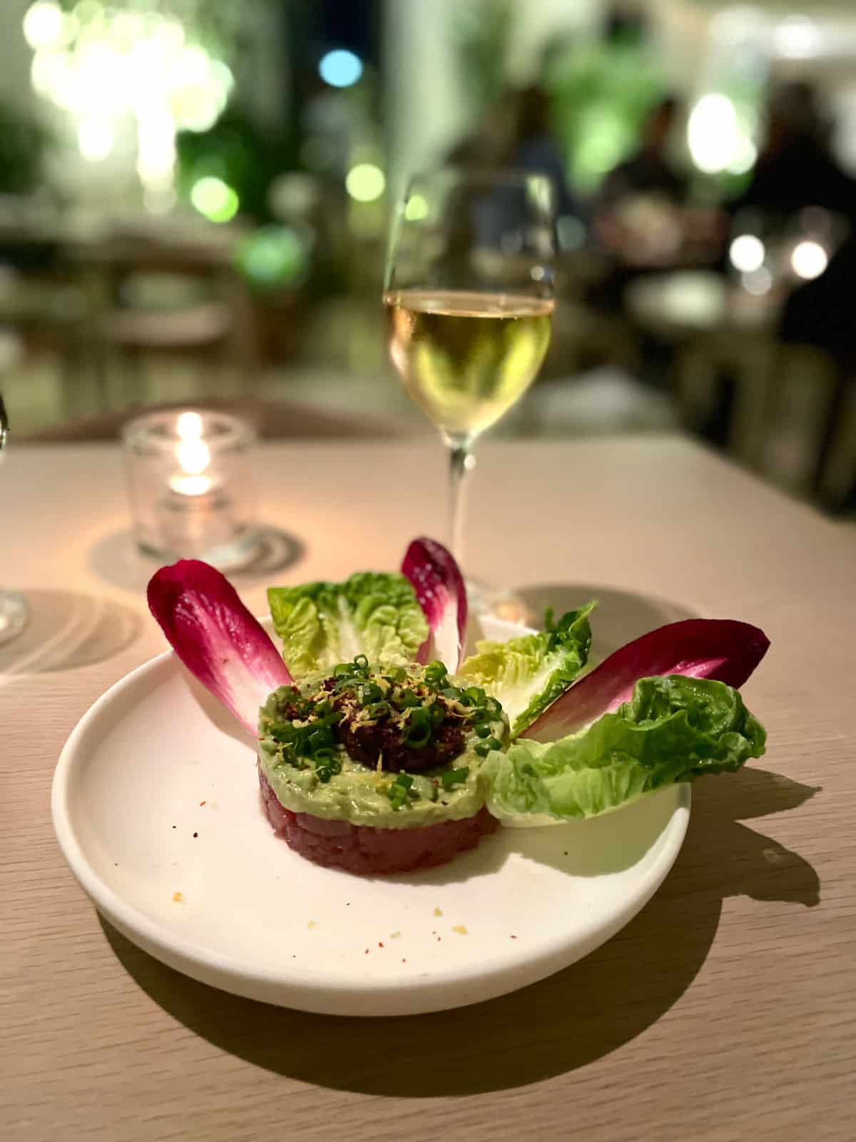 Tuna tartare with avocado and lettuce leaves with white wine in background.