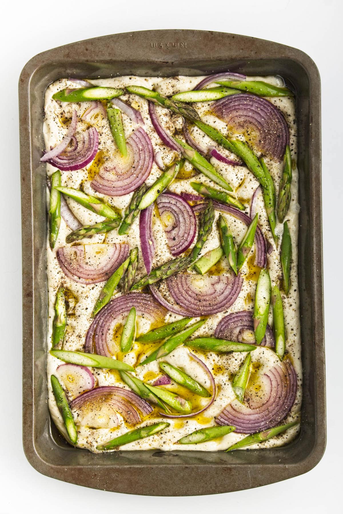 Dough with onion and asparagus in a baking pan.