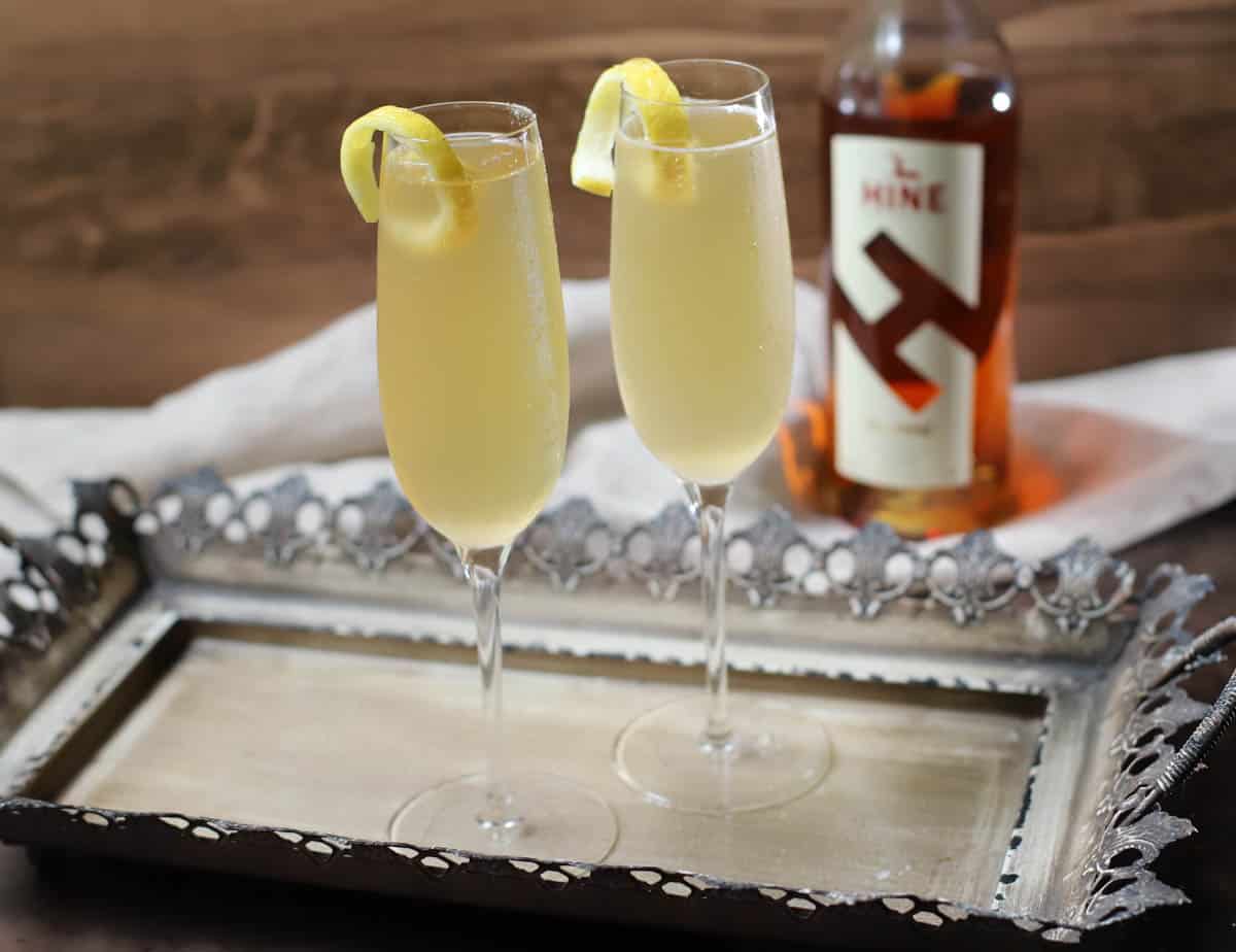French 75 cocktail on a tray with a bottle of cognac in back.