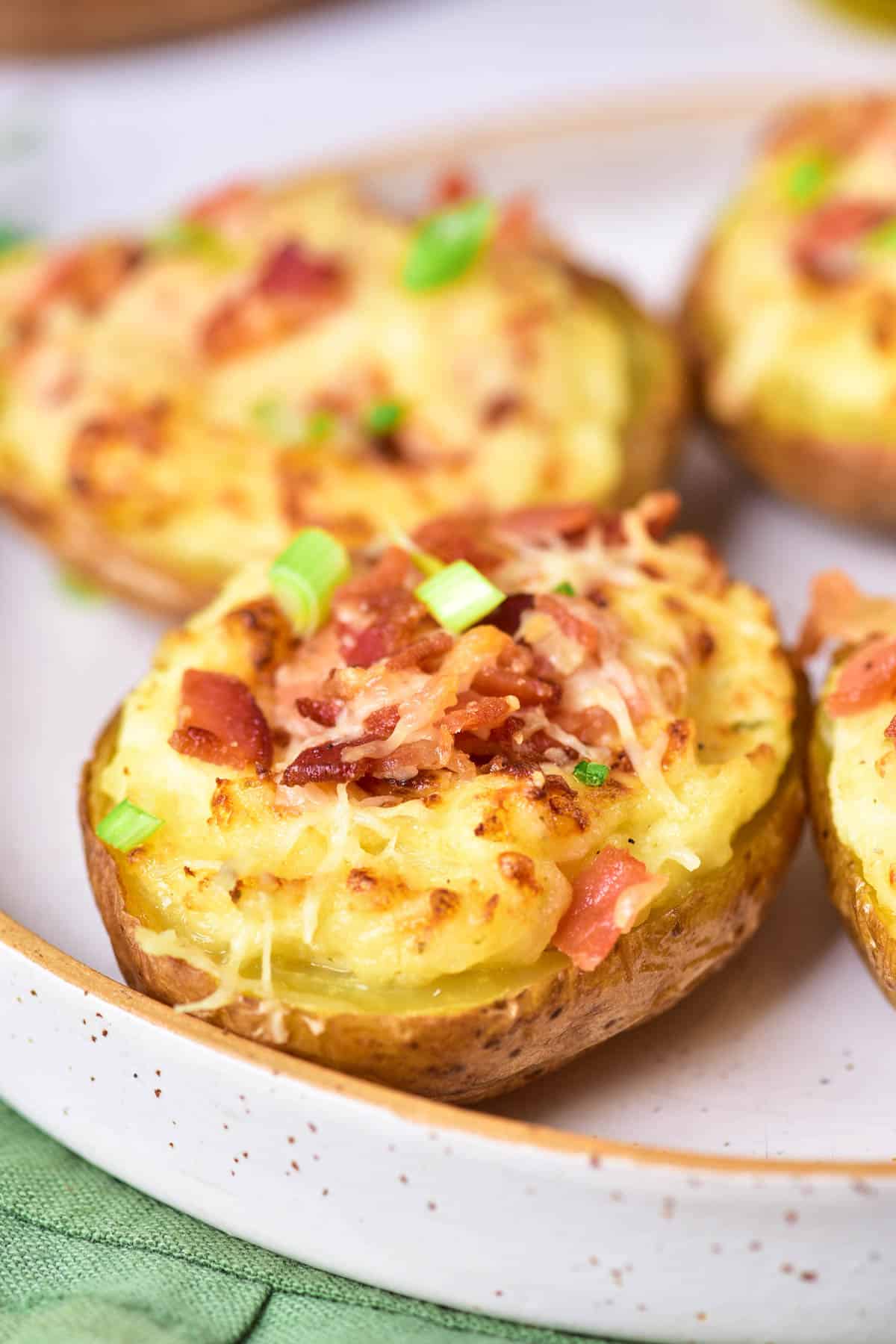 Baked potatoes with sour cream, cheese, green onions, and bacon on a plate.