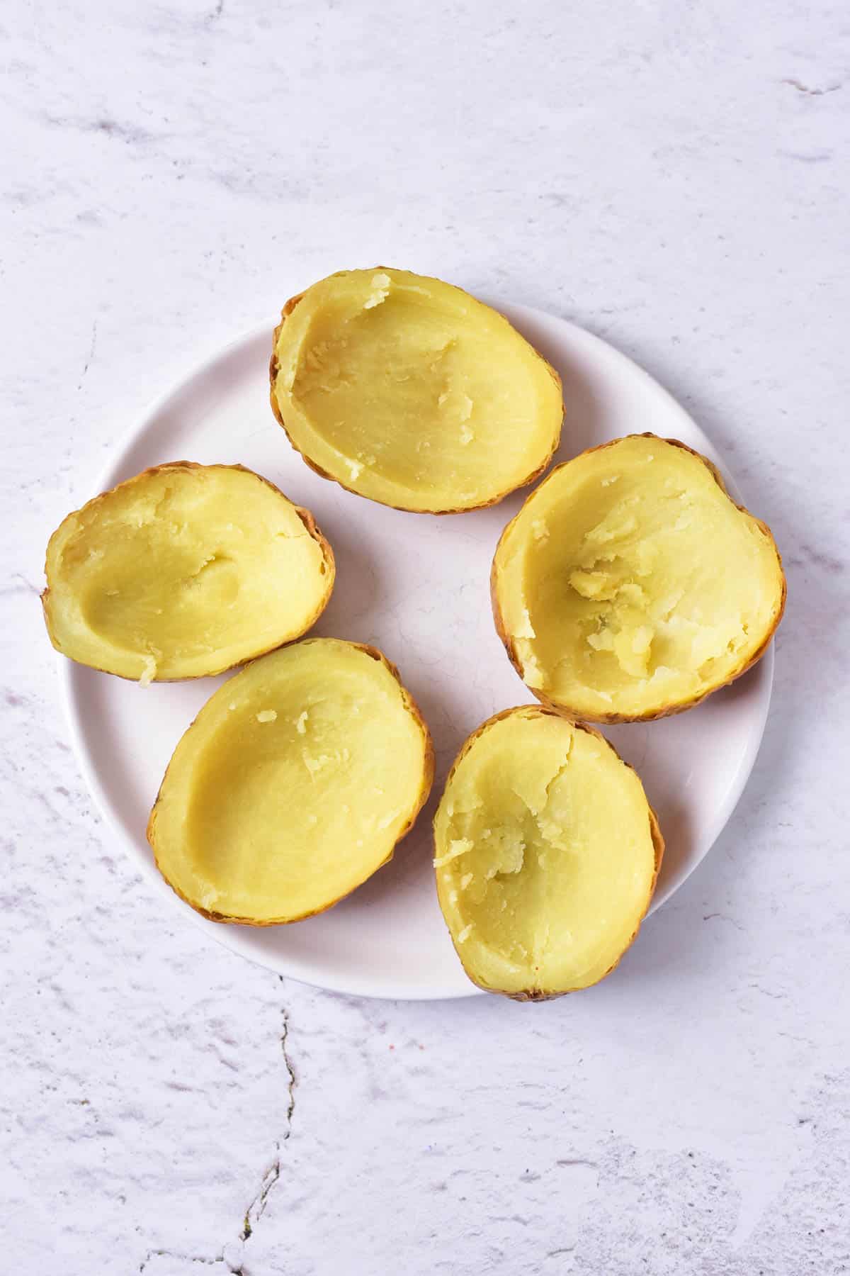 Scooped out baked potato halves on a plate.