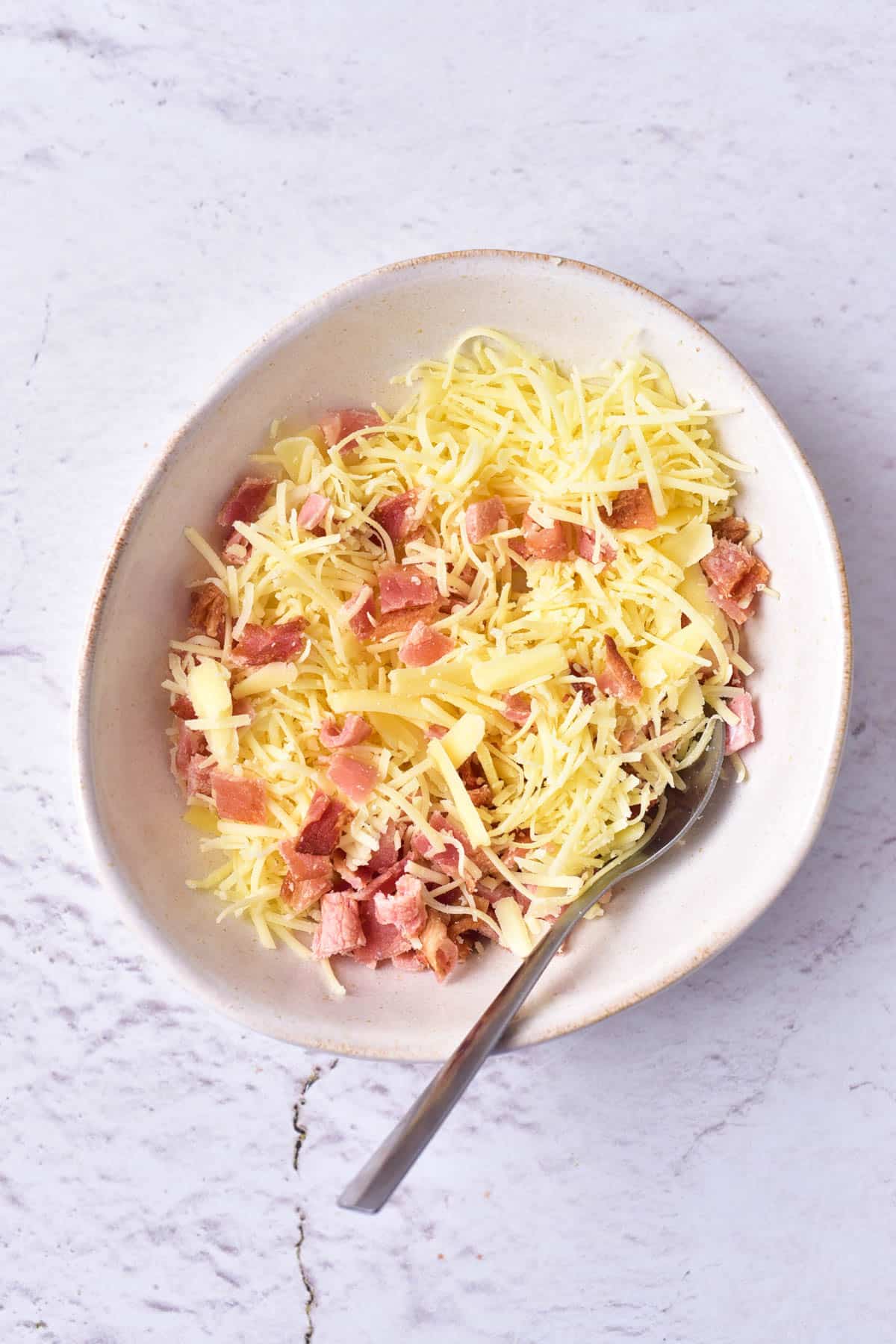 Cheese and bacon in a bowl with a spoon.