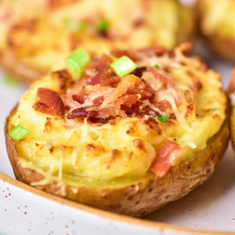 Baked potatoes with sour cream, cheese, green onions, and bacon on a plate.