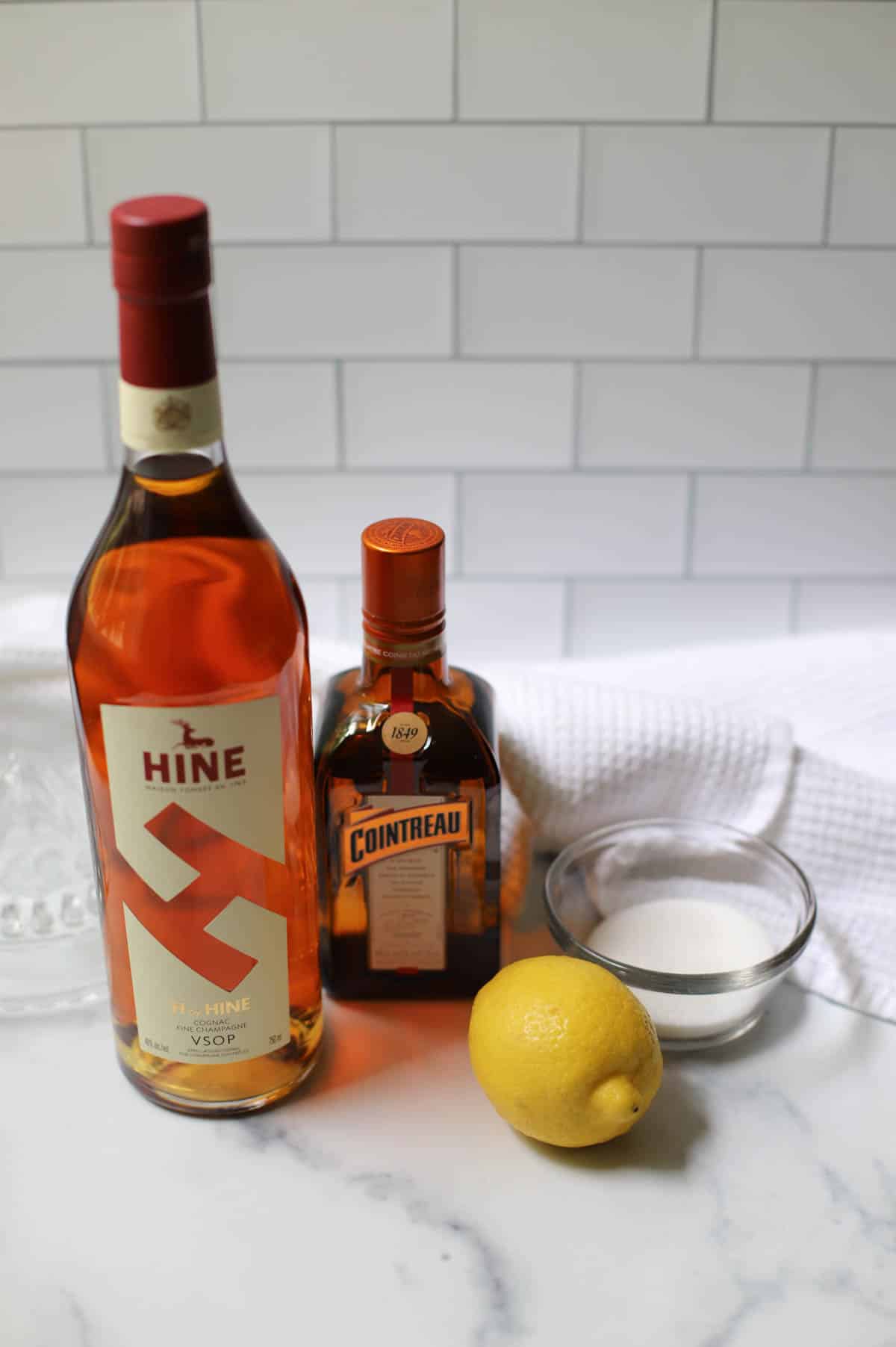 Ingredients for sidecar cocktail on white counter with a white dishtowel.