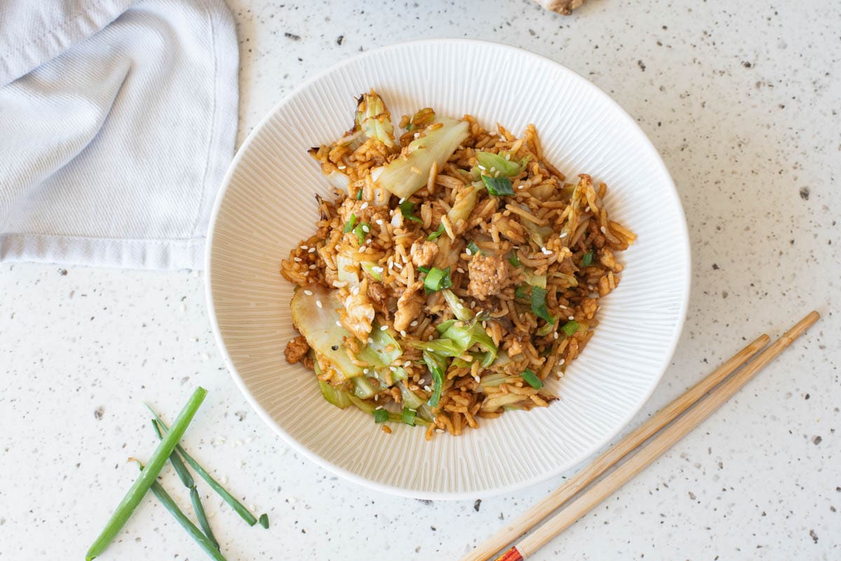 Egg fried rice in a white bowl with chopsticks in front and serving bowl in back.