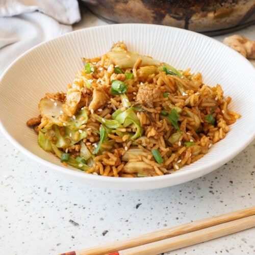 Egg fried rice in a white bowl with chopsticks in front and serving bowl in back.