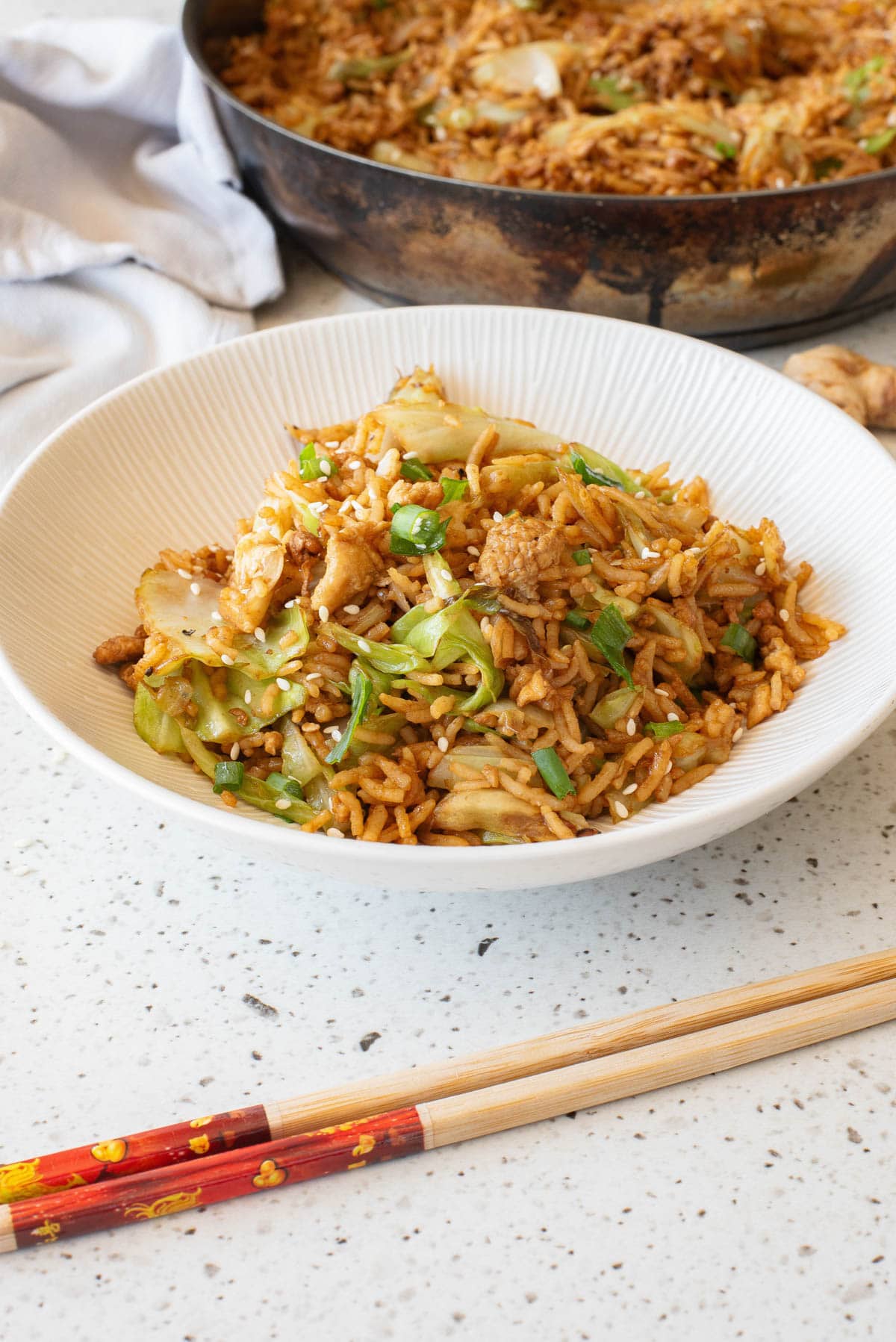 Egg fried rice in a white bowl with chopsticks in front and serving bowl in back.