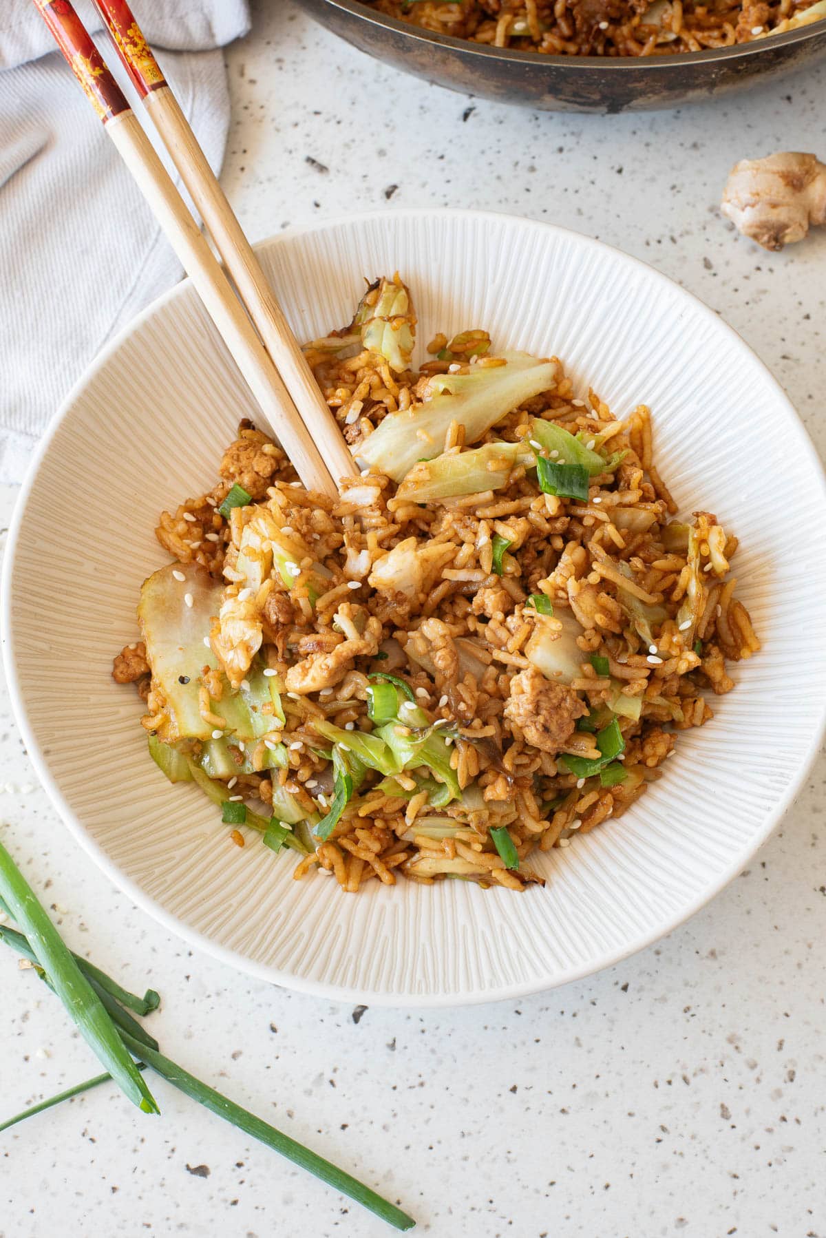 Egg fried rice in a white bowl with chopsticks in front and serving bowl in back.