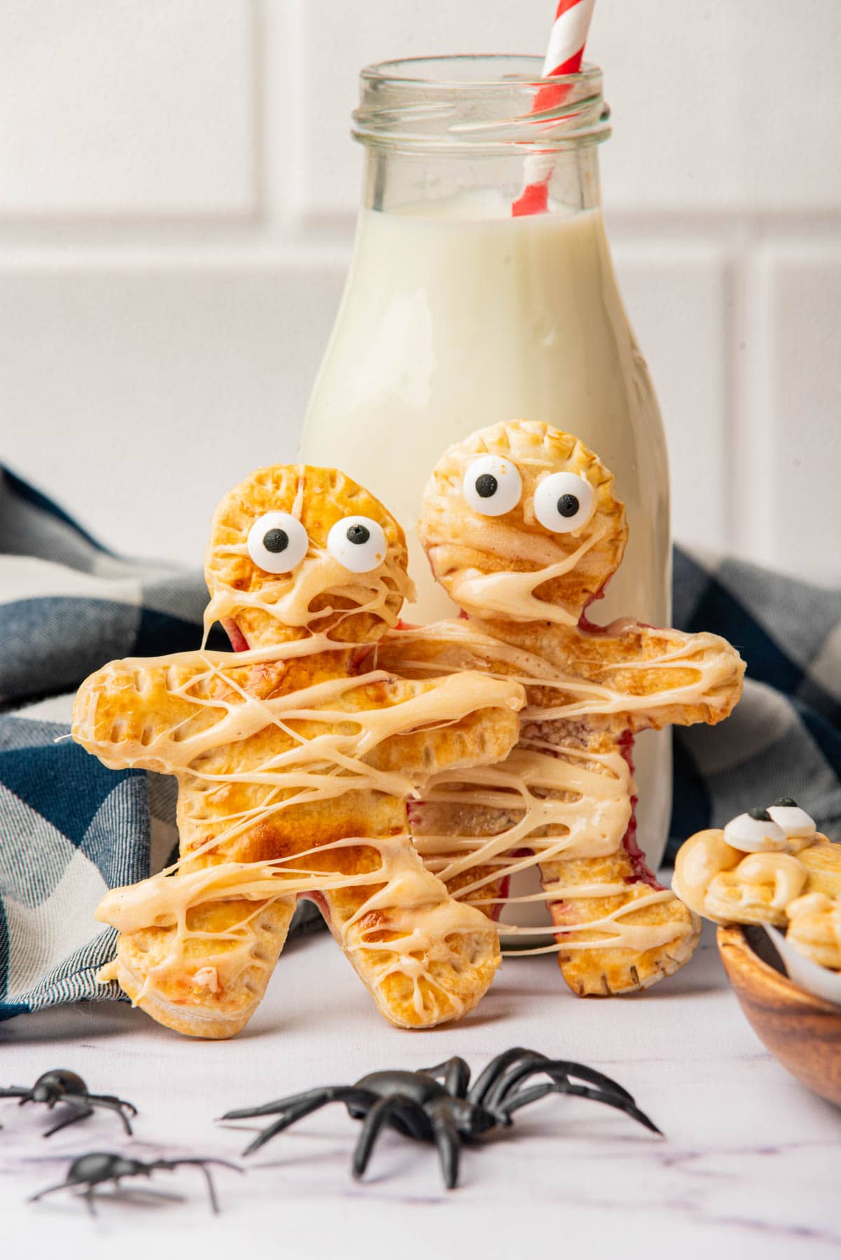 Mummy shaped individual pies with marshmallow drizzle set up against a bottle of milk.