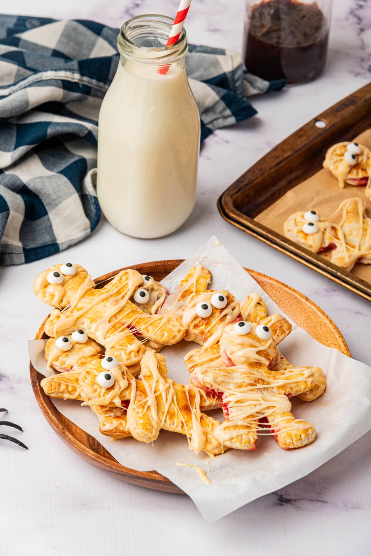 Mummy shaped individual pies with icing drizzle on paper on table with spiders and black and white napkin.