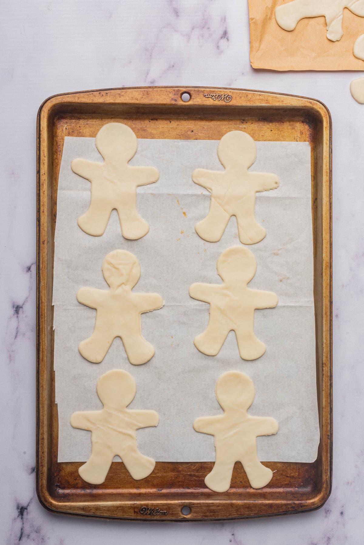 Man-shaped cookies on parchment on a baking sheet.