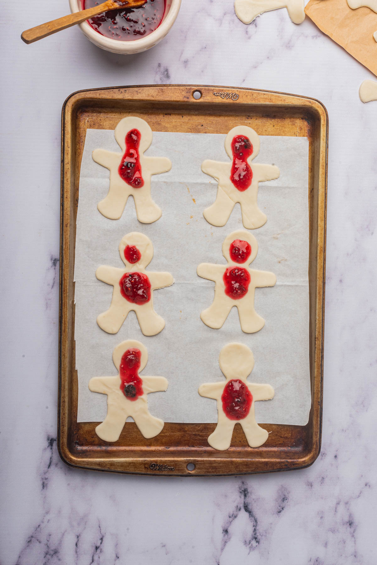 Man-shaped cookies with jam in center on parchment on a baking sheet.