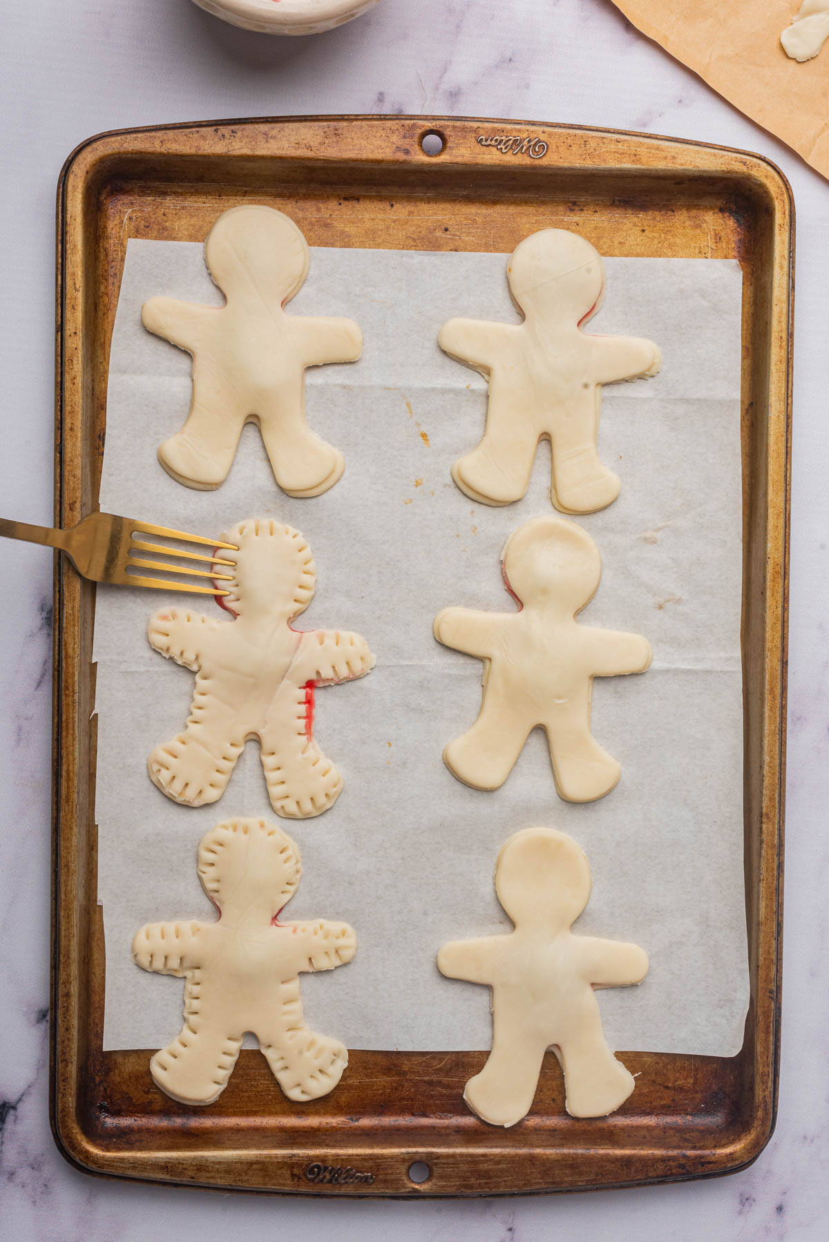 Man-shaped cookies on parchment on a baking sheet with fork sealing sides.