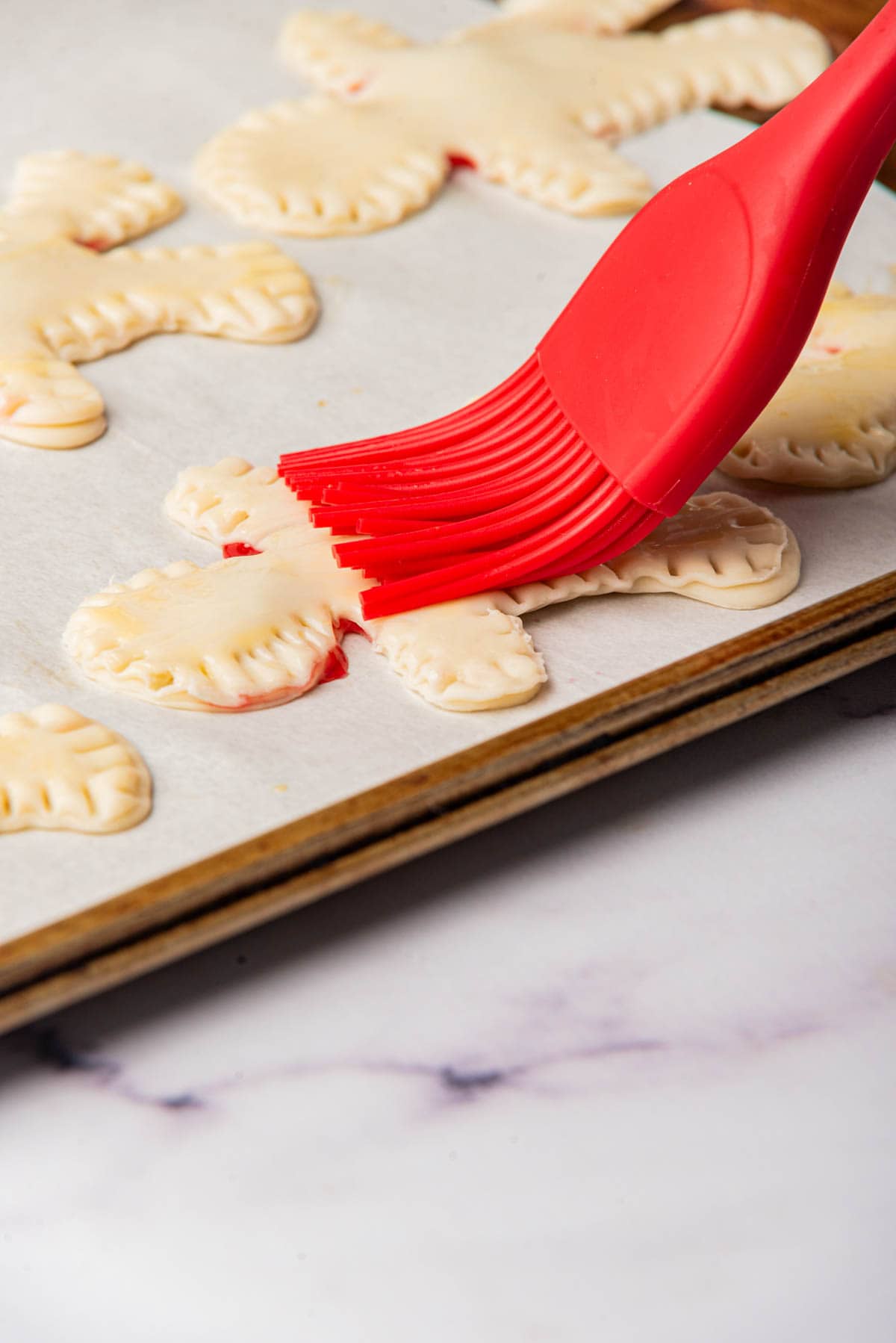 Brushing egg yolk on hand pies on baking sheet.