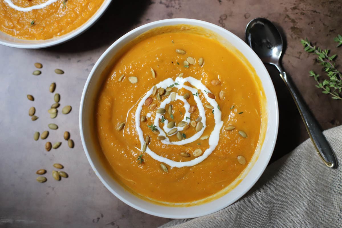 Butternut squash soup topped with sour cream and pepitas in a white bowl on a brown counter.