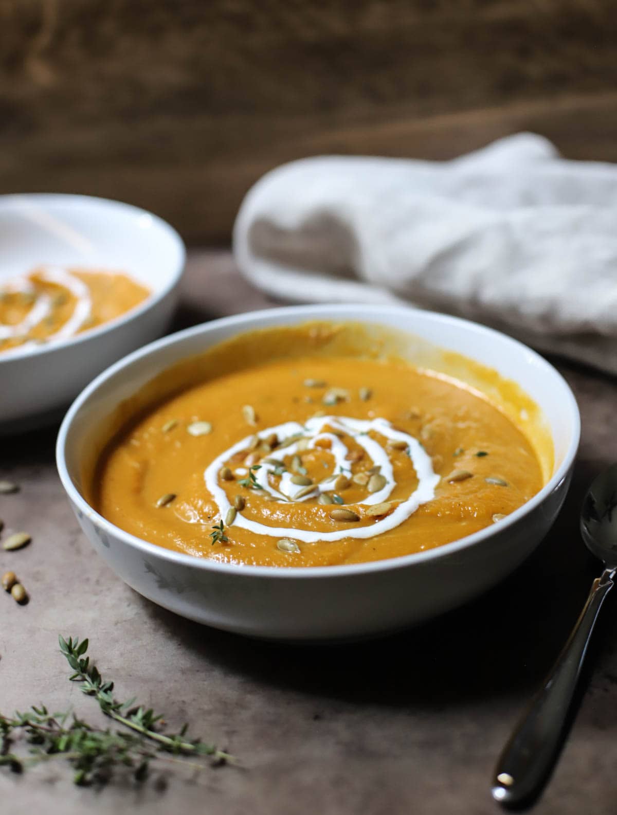 Butternut squash soup topped with sour cream and pepitas in a white bowl on a brown counter.