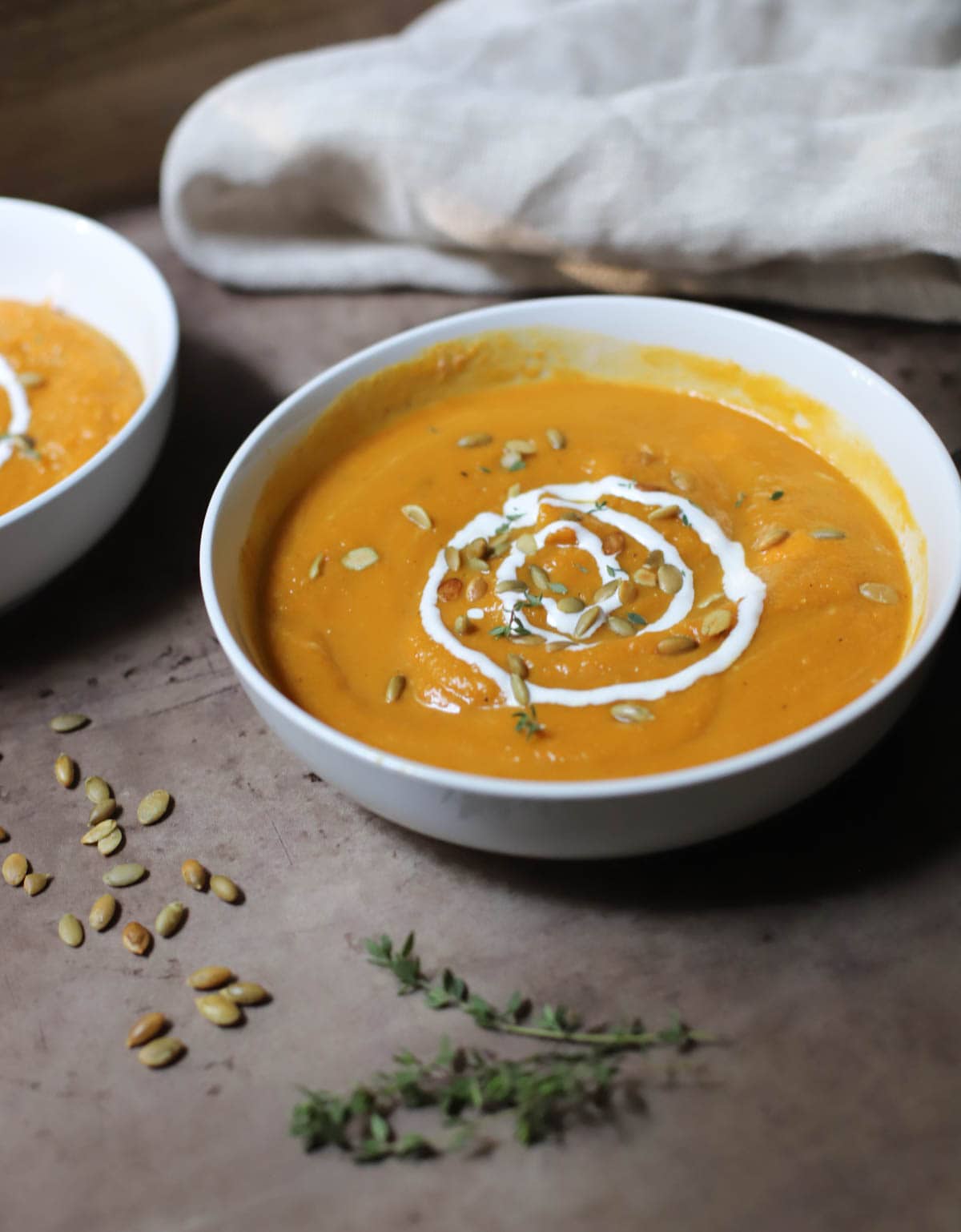 Butternut squash soup topped with sour cream and pepitas in a white bowl on a brown counter.