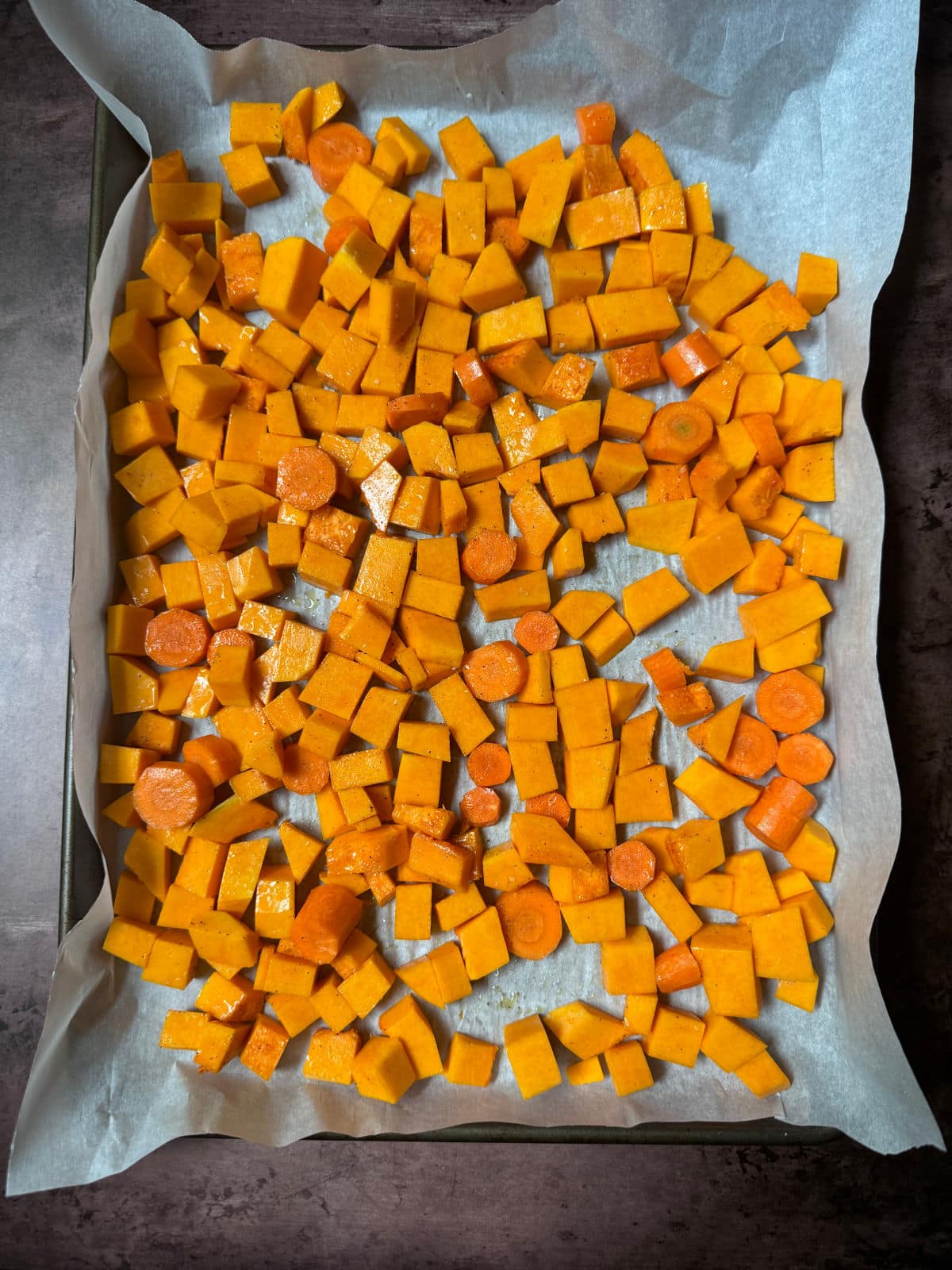 Cubed butternut squash on parchment paper on a baking sheet.