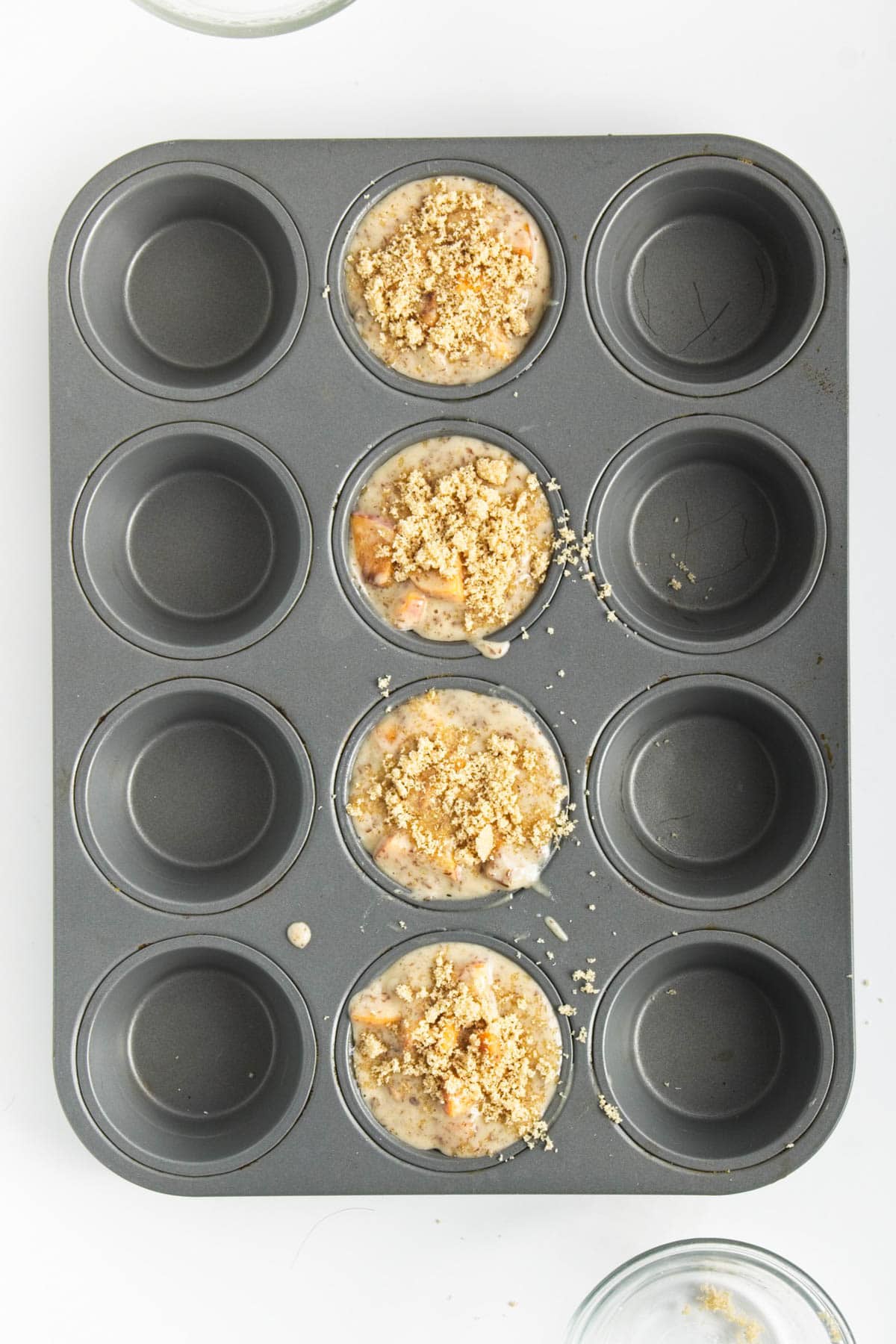 Four unbaked muffins with brown sugar topping in 12 hole muffin tin.