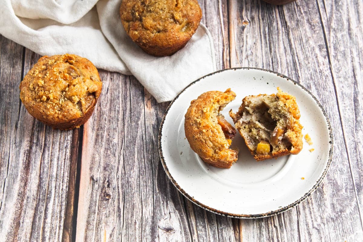 Muffin broken in half on wood table with other muffins in background.