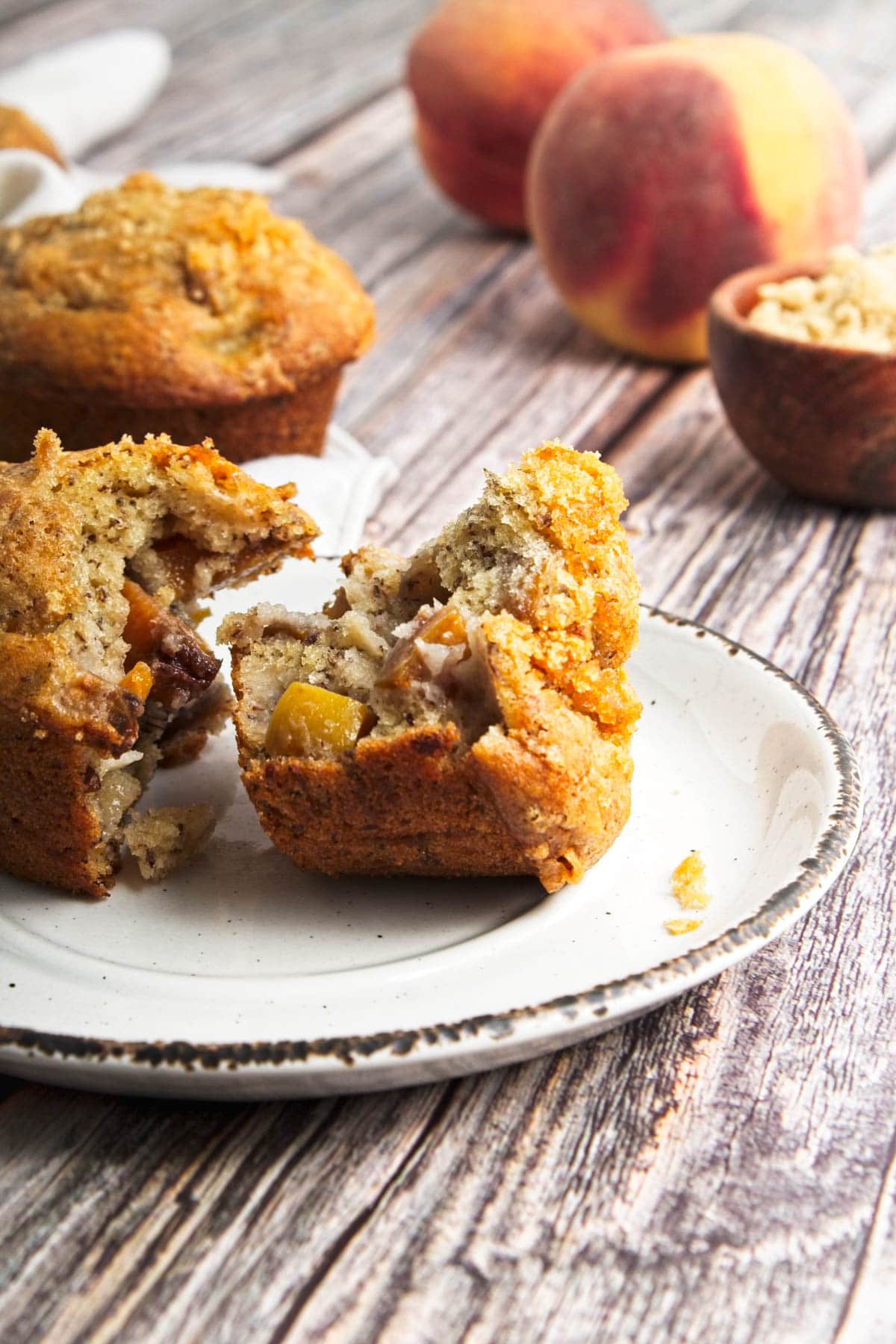 Peach muffin broken in half with another muffin behind and peaches in background.