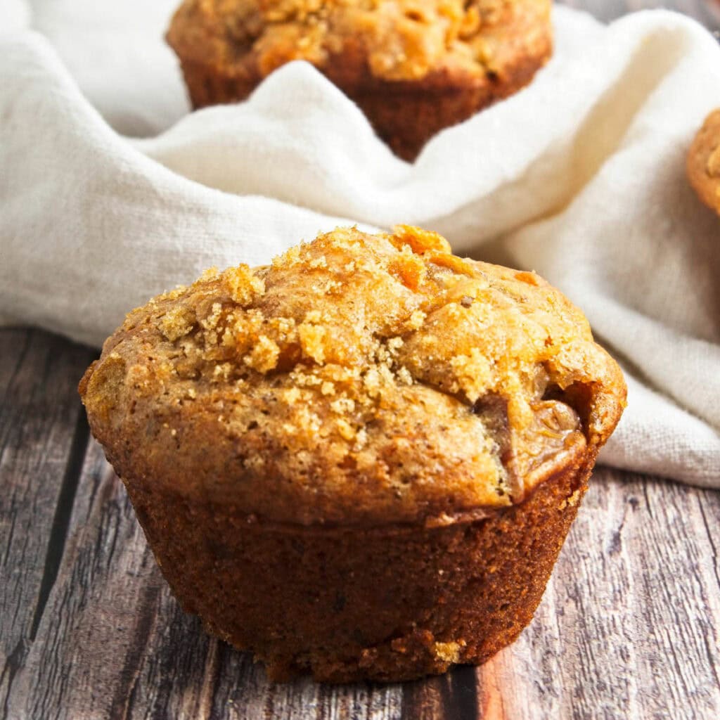 Peach muffin on wood table with another muffin in background.