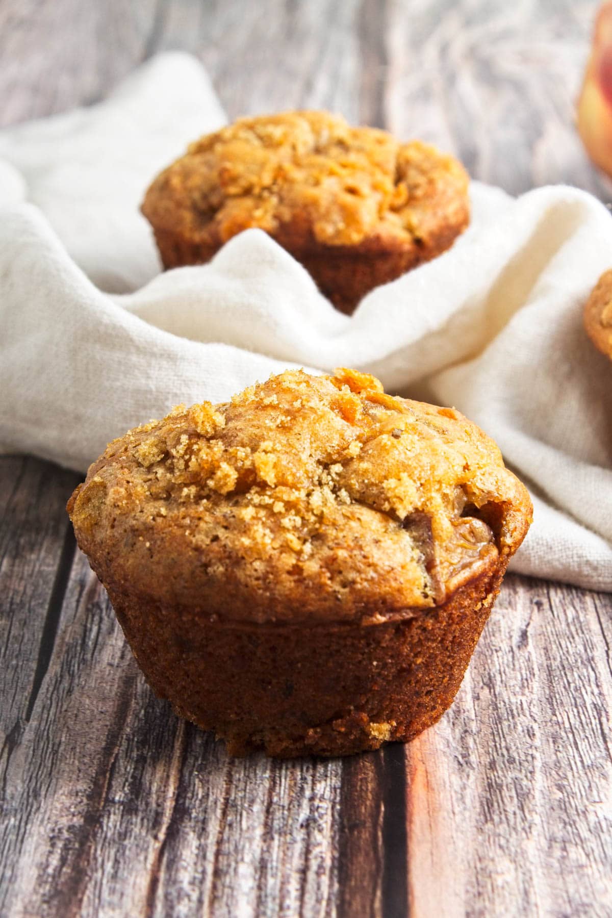 Muffin on wood board with another muffin in napkin in background.