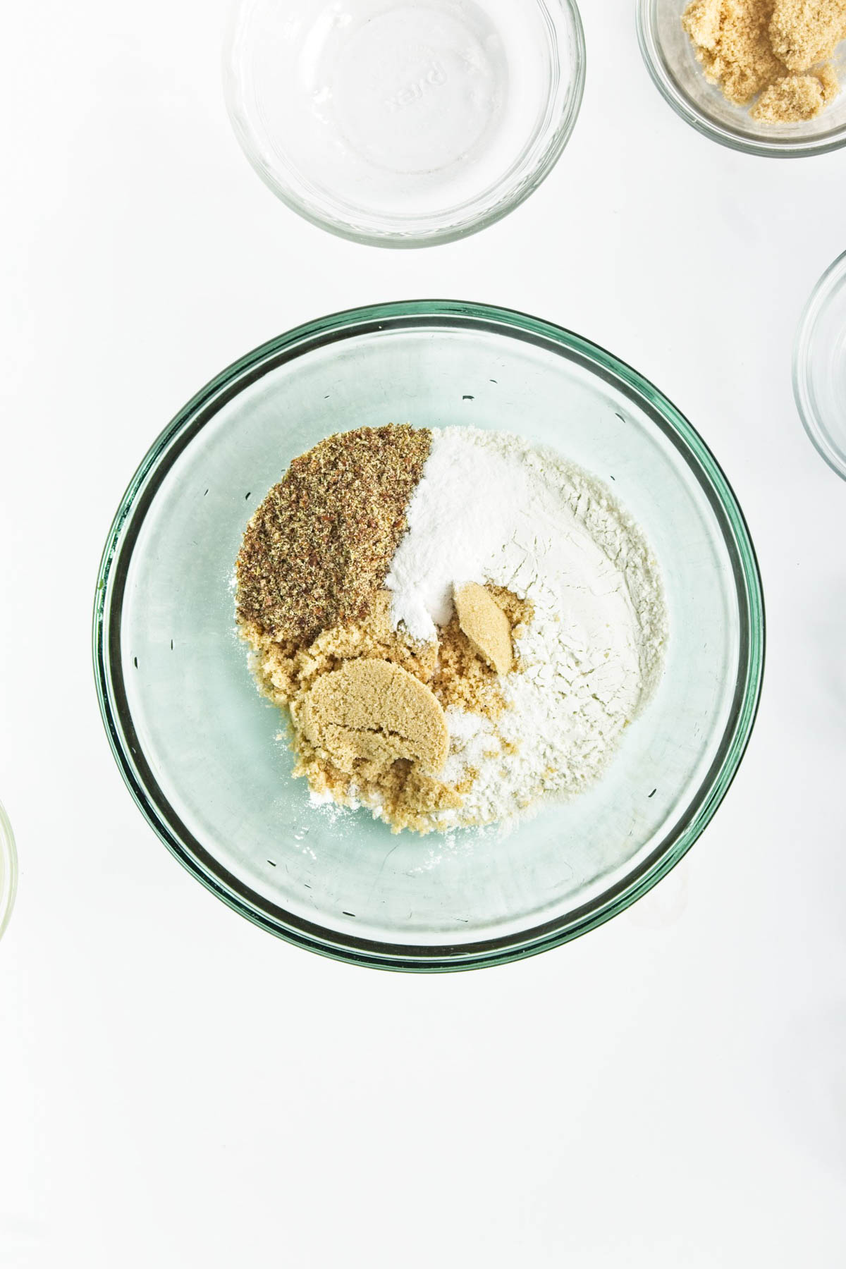 Dry ingredients in a glass bowl with brown sugar in smaller glass bowl in corner.