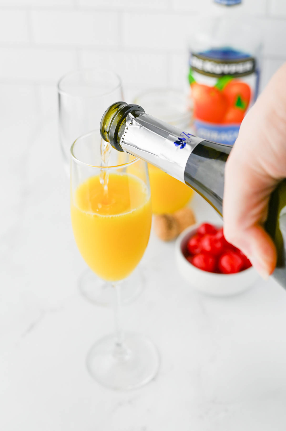 Pouring sparkling wine into glass with orange juice.