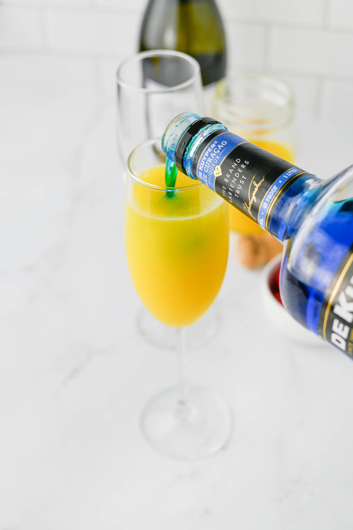 Pouring blue liquid into glass of orange juice.