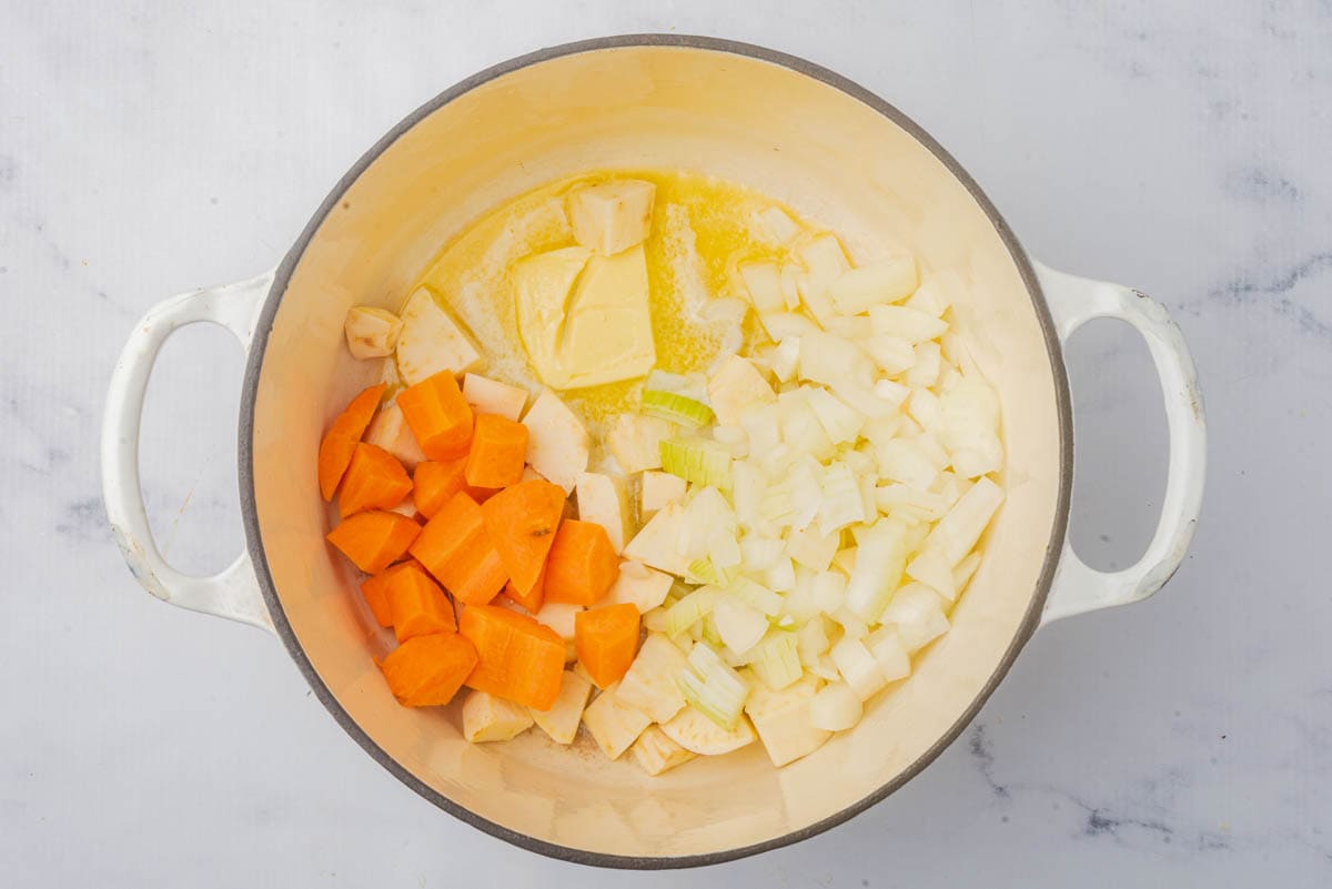 Raw carrots, onion, sweet potato, and butter in a pot.