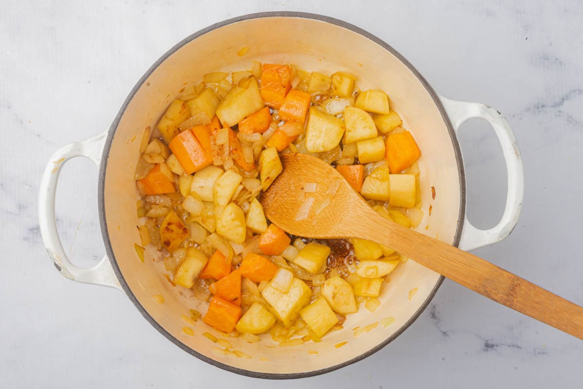 Cooked carrots, onion, sweet potato, and butter in a pot.