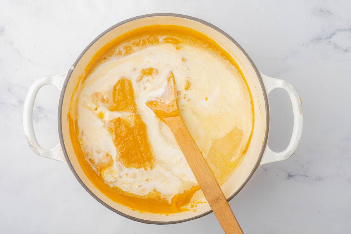 Creamy pumpkin soup with cream in pot with wooden spoon.